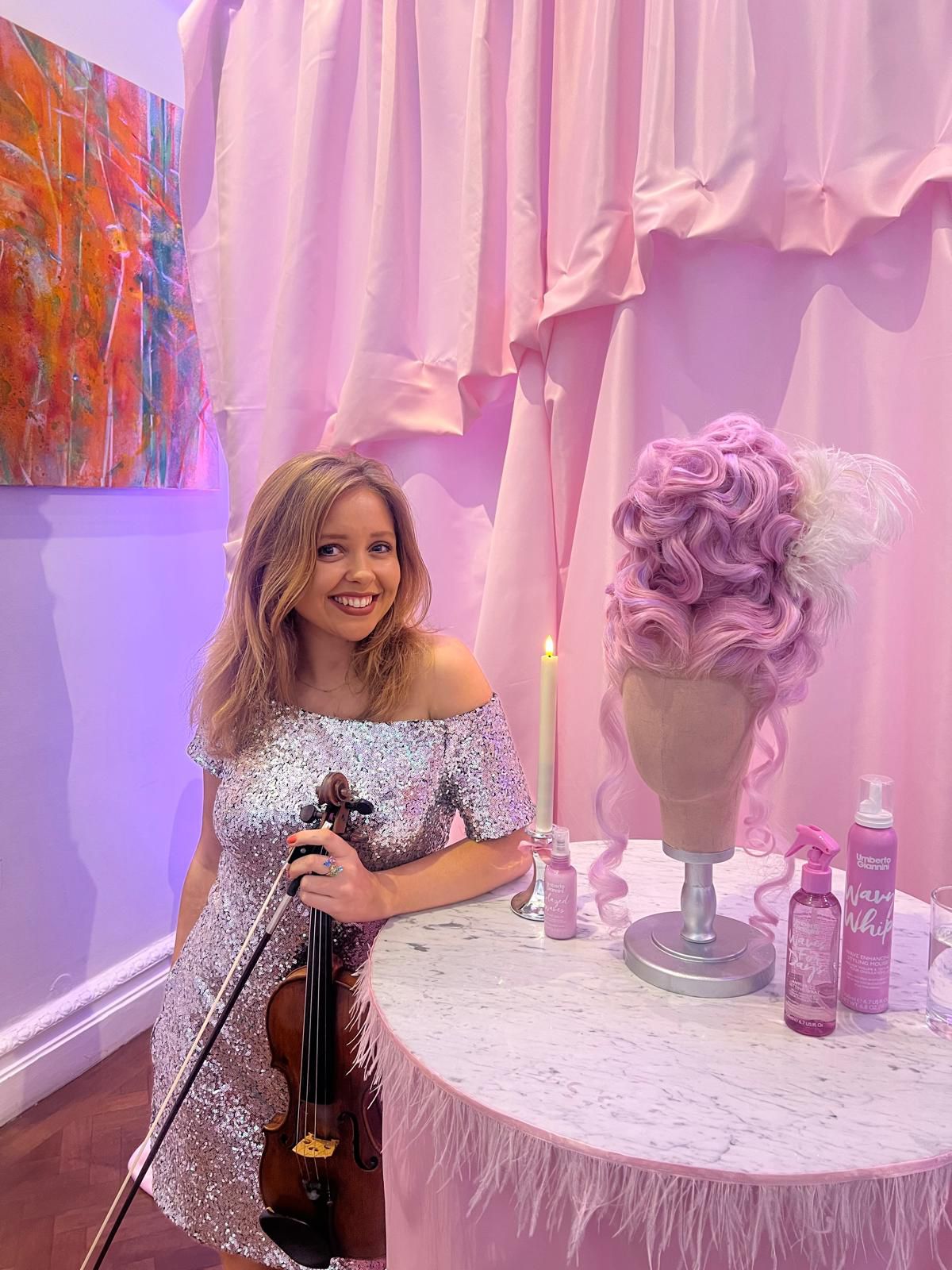 Secret Strings violinist in silver sequin dress performing beside the Umberto Giannini Wavy Whip product display at a Central London launch party